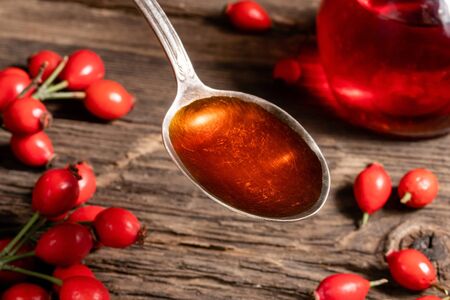 Rose hip seed oil on a vintage spoon, with fresh berries in the backgroundの写真素材