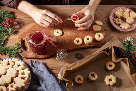 Hands filling traditional Linzer Christmas cookies with red currant jam