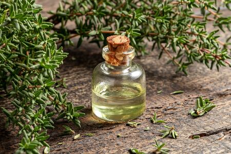 A transparent bottle of essential oil with fresh thyme twigs on a tableの写真素材
