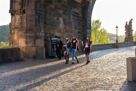 PRAGUE, CZECH REPUBLIC - APRIL 16, 2020: Half-empty Charles Bridge during the coronavirus pandemic, with people in face masksのeditorial素材