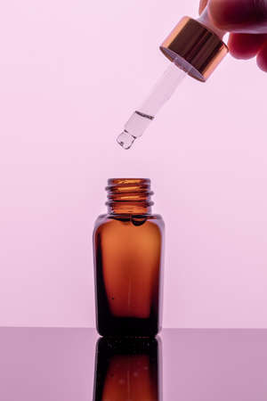 A bottle of essential oil with a dropper on a pink background