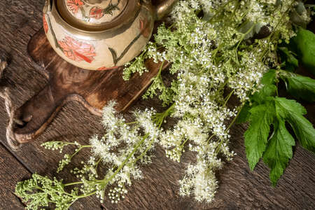 Blooming meadowsweet twigs with a teapot on a table