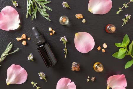 Bottles of essential oil with frankincense, rose petals, oregano, creeping thyme and other herbsの写真素材