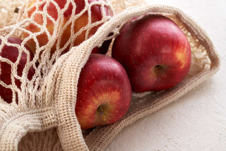 Closeup of red apples in an ecological reusable mesh bag made of organic cotton on a white...