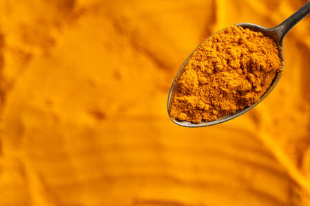 Turmeric powder on a metal spoon, top view with copy space