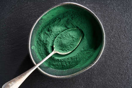 Spirulina powder in a black bowl, top view