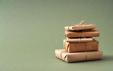 A stack of Christmas presents wrapped in ecological recycled paper on green background with copy spaceの写真素材
