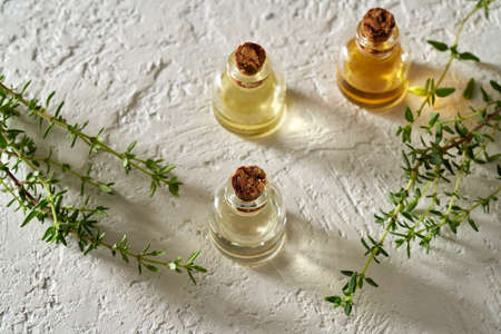 Three bottles of essential oil with fresh thyme twigs on white backgroundの写真素材