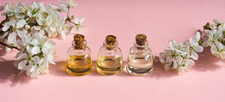 Panoramic header with three bottles of essential oil on pink background with spring blossoms