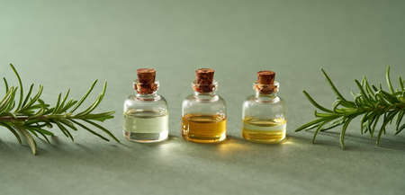 Three essential oil bottles with fresh rosemary twigs on green background with copy spaceの写真素材