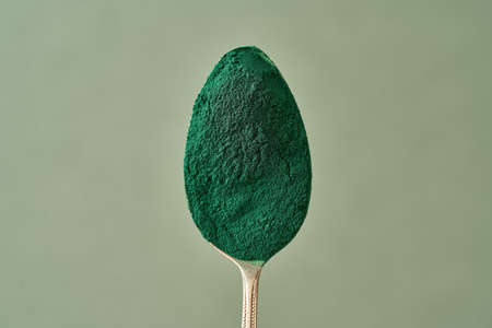 Spirulina powder on a spoon above a green background with copy spaceの写真素材