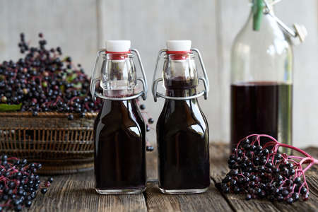 Black elder syrup in two bottles with fresh elderberries on a tableの写真素材