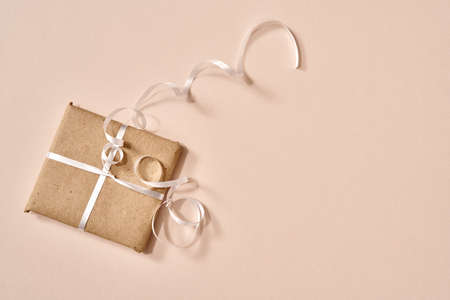 Christmas present wrapped in ecological recycled paper on champagne colored background with copy spaceの写真素材
