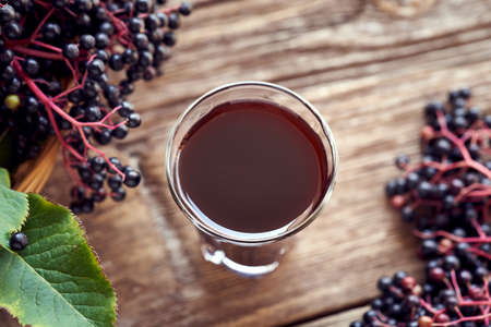 A glass of black elder syrup with fresh elderberries on a tableの写真素材