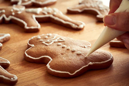 Hand decorating homemade gingerbread Christmas cookies with a cone - preparation of traditional...