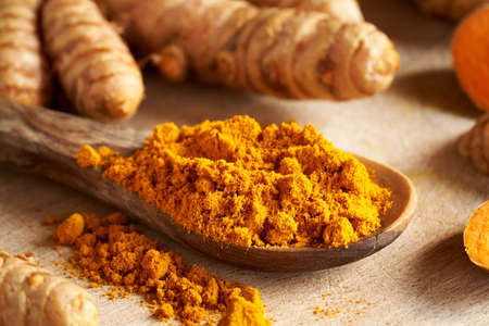 Turmeric powder on a wooden spoon with fresh root in the backgroundの写真素材