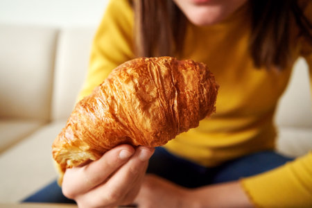 Fresh croissant in the hand of a girl having breakfast, close upの写真素材