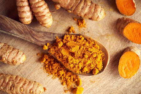 Curcuma powder on a spoon with fresh whole and cut up turmeric root, top view