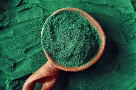 Green spirulina algae powder on a wooden spoon, top view