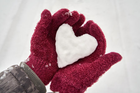 Female hands in purple gloves holding a snow heart - Valentine's day or love concept