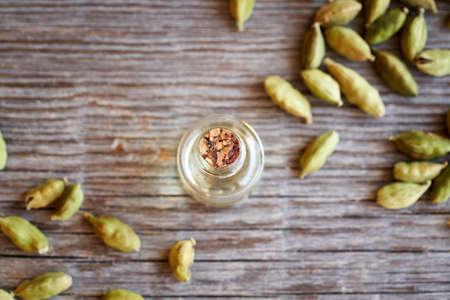 A bottle of aromatherapy essential oil with whole cardamom seeds on a wooden background, top viewの写真素材