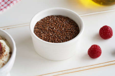 Flax seeds in a white bowl with fresh berries on white background