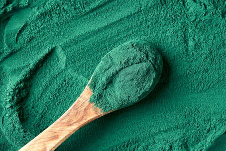 Spirulina algae powder on a wooden spoon on green background, top view