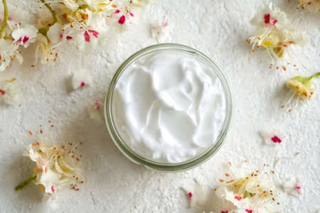 A jar of ointment made from fresh horse chestnut flowers on white background, top view