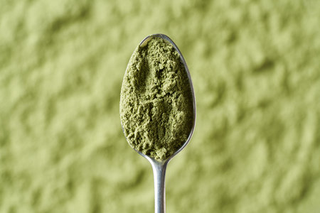 Dry barley grass powder on a spoon over green background - healthy nutritional supplement