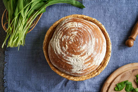 A loaf of homemade sourdough bread in a basket, with fresh wild garlic leaves collected in spring,...