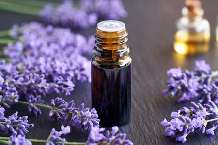 A brown bottle of essential oil with fresh blooming lavender twigs on a gray backgroundの写真素材