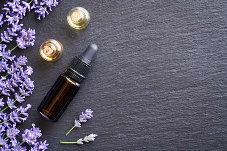 Dark background with bottles of essential oil with fresh blooming lavender, top viewの写真素材