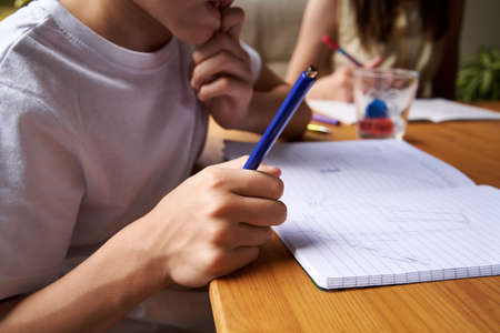 Boy thinking and drawing into an exercise book at a table at homeの写真素材