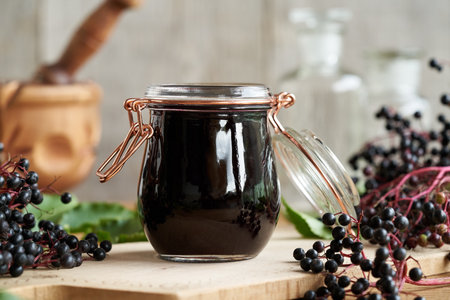 A jar of homemade black elder syrup with fresh elderberries on a wooden tableの写真素材