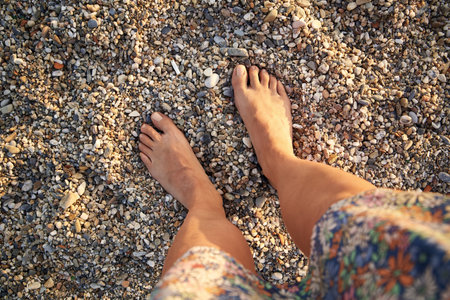 Woman standing barefoot on pebbles at the beach at sunset, top viewの写真素材