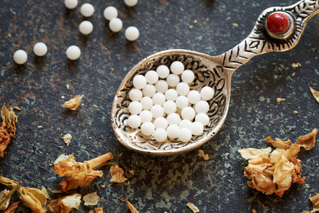 Homeopathic globules on a metal spoon with dried herbs. Alternative medicine.