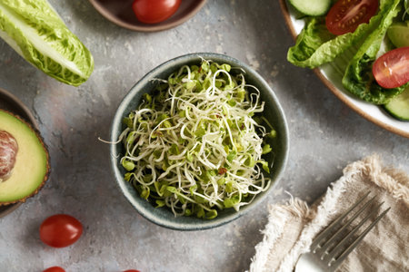 Radish sprouts in a bowl with a vegetable salad in the backgroundの写真素材