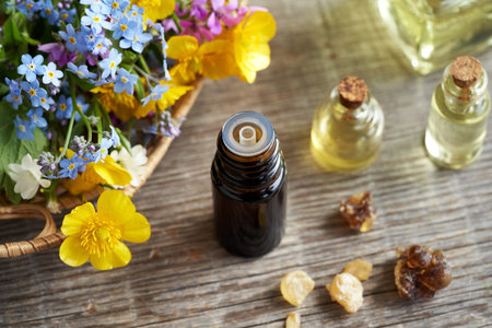 A dark bottle of aromatherapy essential with frankincense resin and spring flowers in the backgroundの写真素材