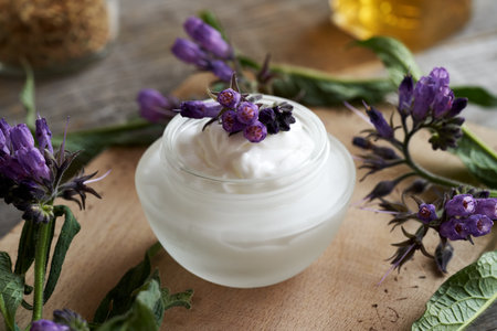 A glass jar of comfrey root ointment with fresh blooming symphytum plantの写真素材