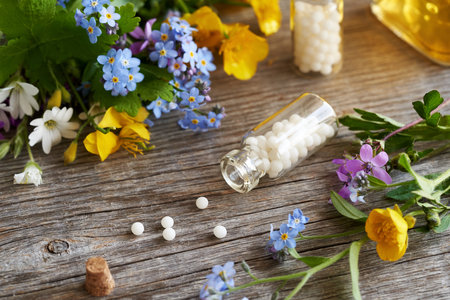 Homeopathic pills spilled from a glass bottle, with fresh colorful flowersの写真素材