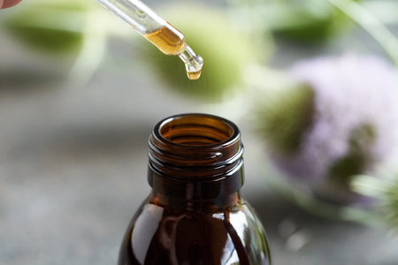 Dropping herbal tincture into a glass bottle, with fresh wild teasel flowers in the backgroundの写真素材