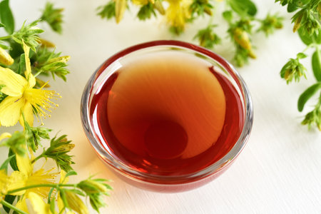A bowl of red oil made from St. John's wort flowers on white backgroundの写真素材