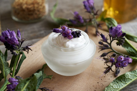 A jar of comfrey ointment with blooming knitbone or comfrey plant