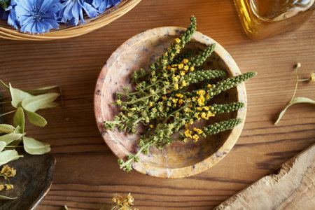 Dried agrimony flowers in a bowl on a table, with chicory and linden flowers in the background