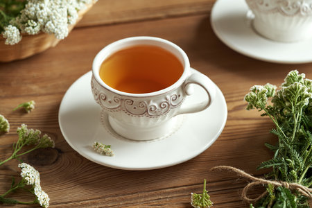 A cup of herbal tea with fresh yarrow flowers on a wooden tableの写真素材