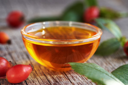 A bowl of rose hip seed oil with fresh rosehips on a tableの写真素材