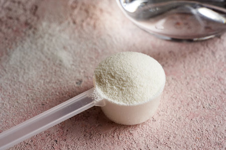 Collagen powder in a plastic measuring spoon on pink backgroundの写真素材