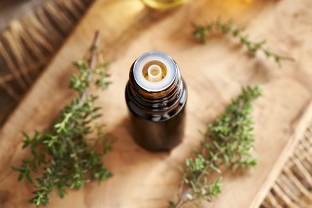 A dark bottle of aromatherapy essential oil with fresh thyme plant on a wooden tableの写真素材