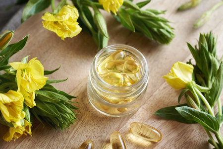 A glass jar with gel capsules of evening primrose oil with blooming Oenothera biennis plant. Nutritional supplement.の写真素材
