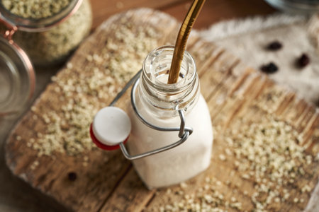 Vegan hemp seed milk in a glass bottle with an ecological stainless steel straw on a tableの写真素材